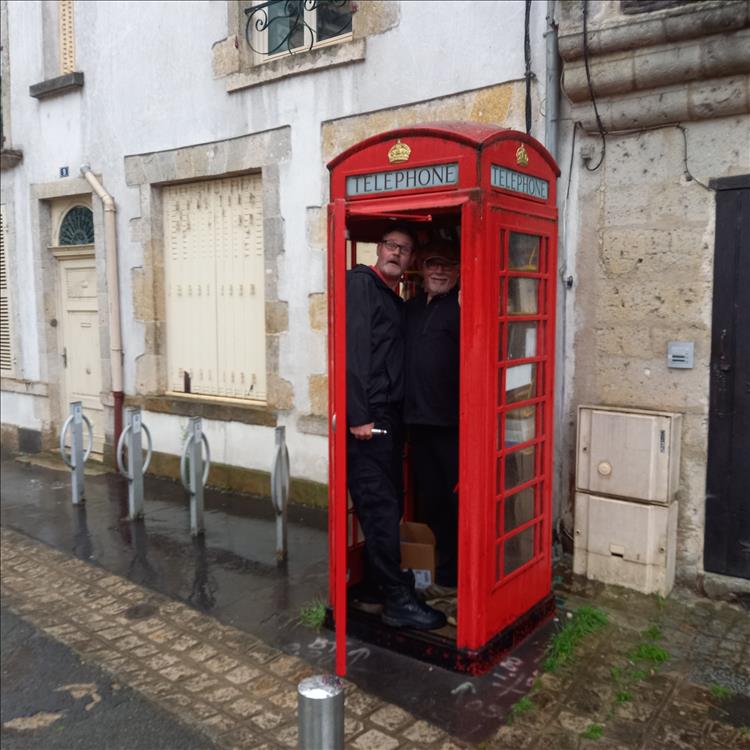 2 friends larking around inside a red British phone box in the French town