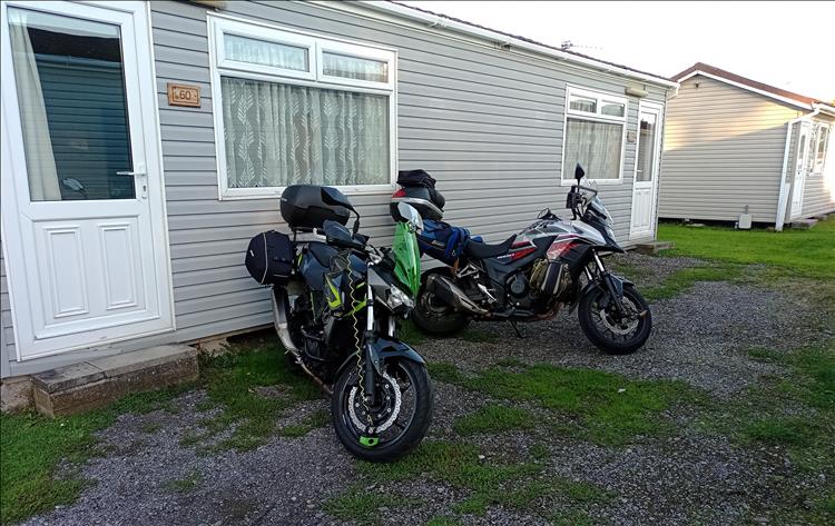 A simple lodge with the 2 bikes parked outside on a gravel surface