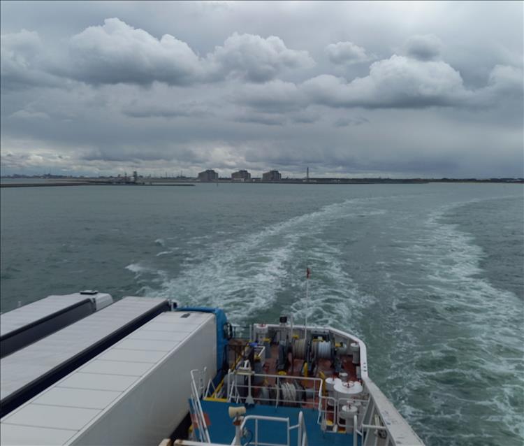 The deck at the back of the ferry, the wake from the ferry and the port in the distance