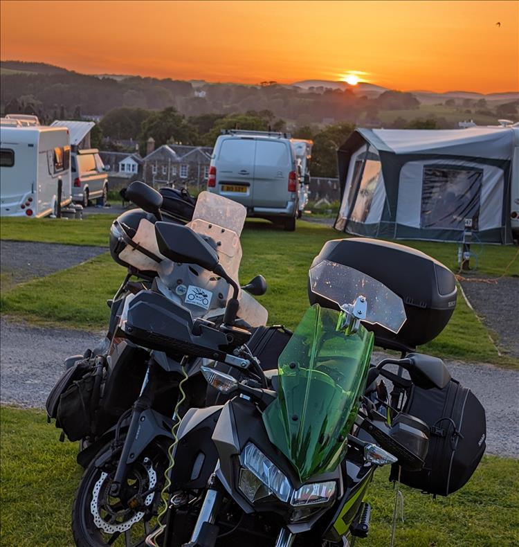 A deep orange sunset behind hills and the town of Kirkcudbright with the motorcycles in the foreground