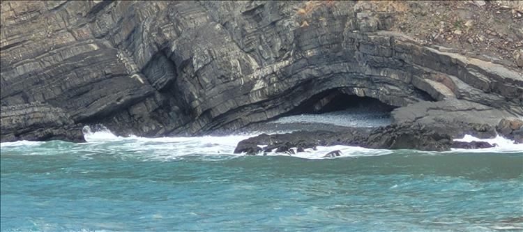 Layers or rock are bent and bowed to form a flat cave by the water's edge