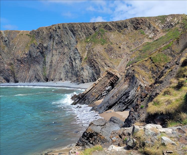 Rocks with layers at all angles, the sea, steep cliffs and sand at Hartland Quay