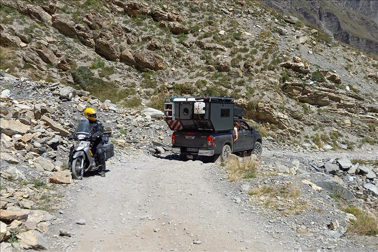 On a rocky and gravel road a small innova 125 passes a large 4x4 overlander truck