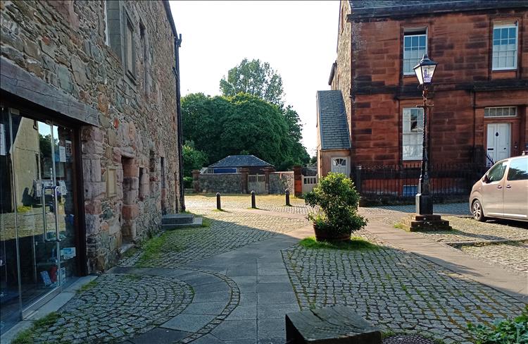 Stone building with modern glass door next to dark red stone building and cobbled street