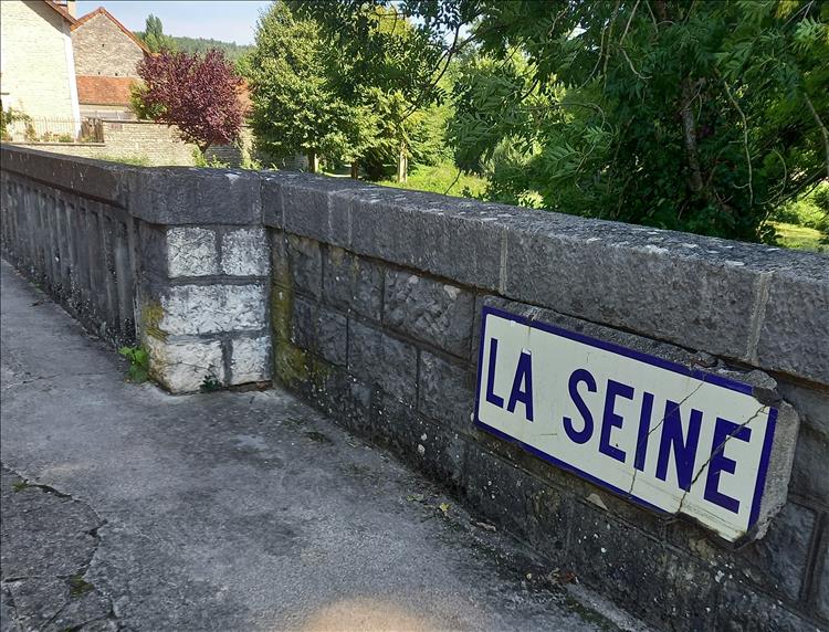 A street sign stating La Seine on a sone bridge on prett countryside