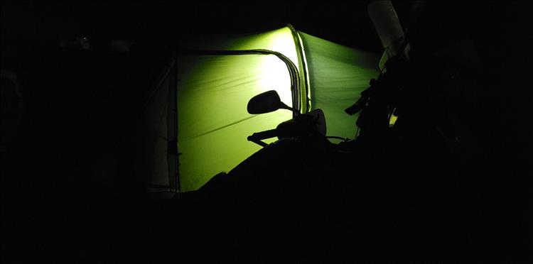 The tent is lit from within producing a green haze against which we can just make out the outline of a motorcycle
