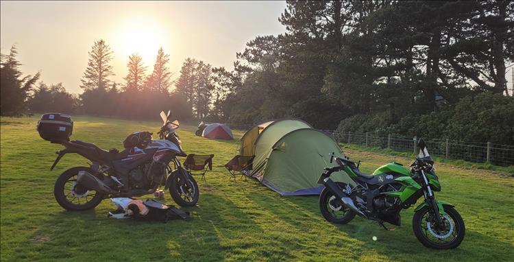A gorgeous sunset behind the tents, motorcycles and trees at Castle Cary