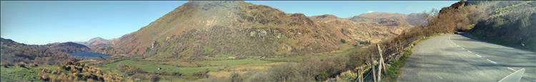 A super wide but narrow scene of mountains and a Llyn in the sunshine in Wales