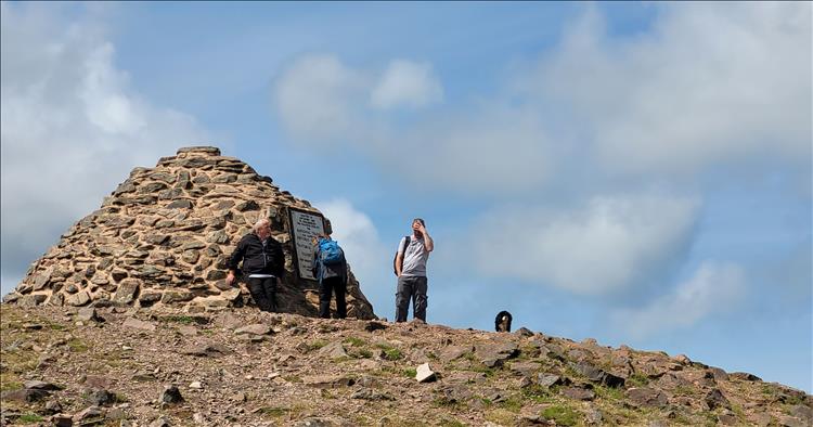 3 people next to a large cairn atop of Dunkery Beacon in the sun