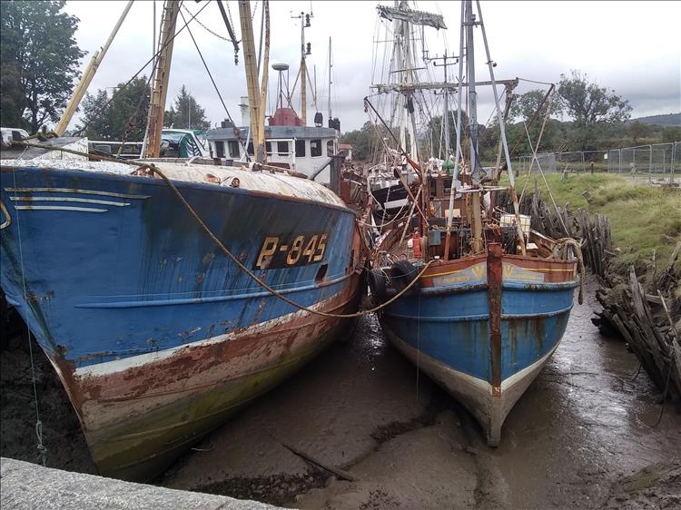 Rusting smaller trawlers on the presently tide out narrow harbour