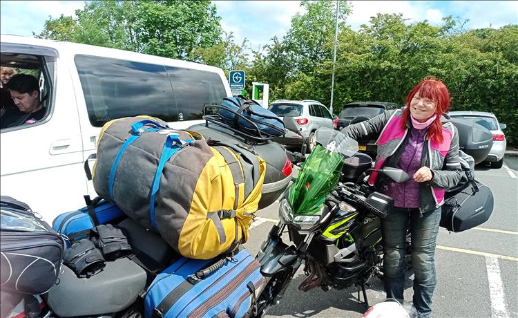 Sharon in a car park next to her motorcycle smiling and laughing in the sunshine