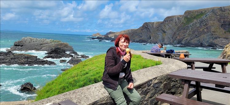 Sharon smiles at the camera with an ice cream in her hand, the sea and the impressive rock formations behind her