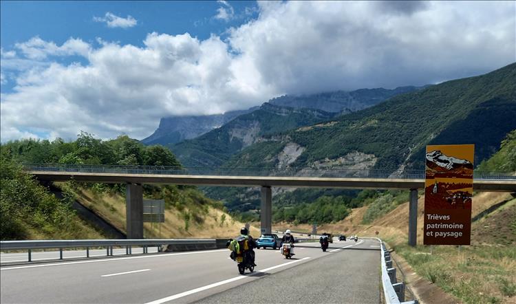 small bikes loaded with camping kit on a dual carriageway and the majestic mountains of the alps