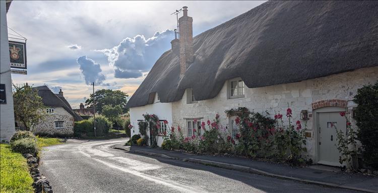 Thatched roofs of old cottages in the street of Ashbury, curious cloud formations too