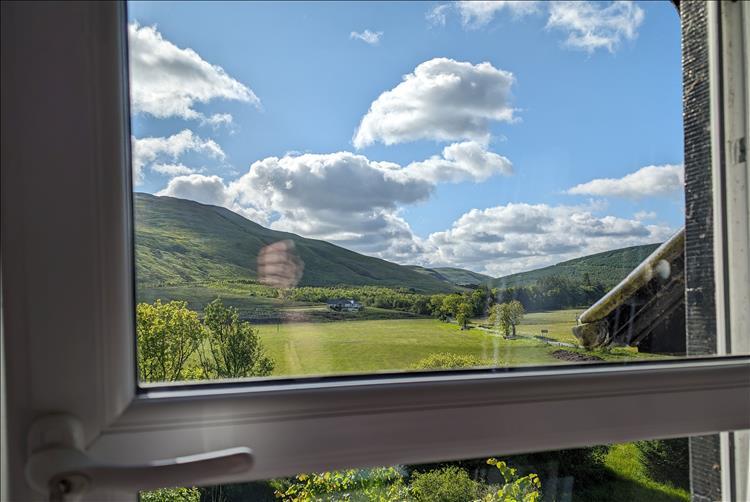 Looking through a window we see rolling hills a verdant green fields in The Borders