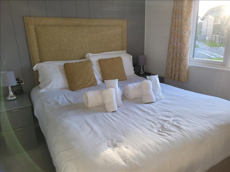 Towels rolled neatly on the freshly made bed in the clean bedroom of the smart lodge