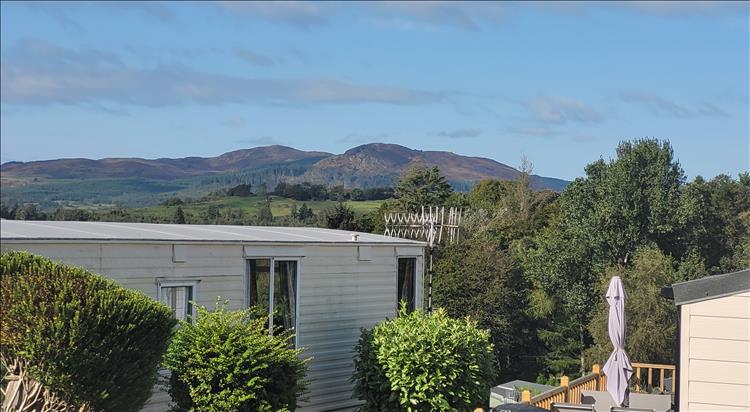 Across the top of a few static caravans we see a big angular hill and trees around the base