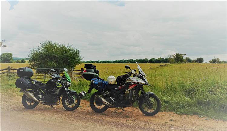 2 motorcycles beside a very typical farm field with long grasses, stone walls and trees