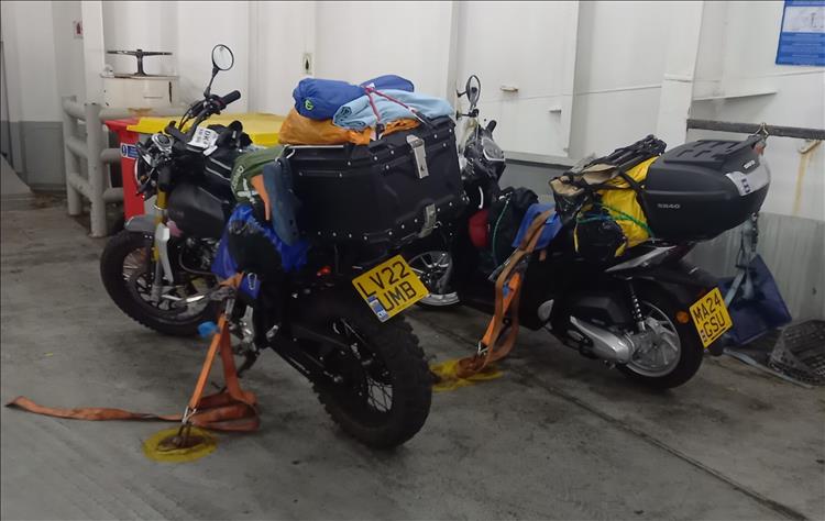 2 125cc motorcycle laden with camping luggage strapped down in the hold of a ferry