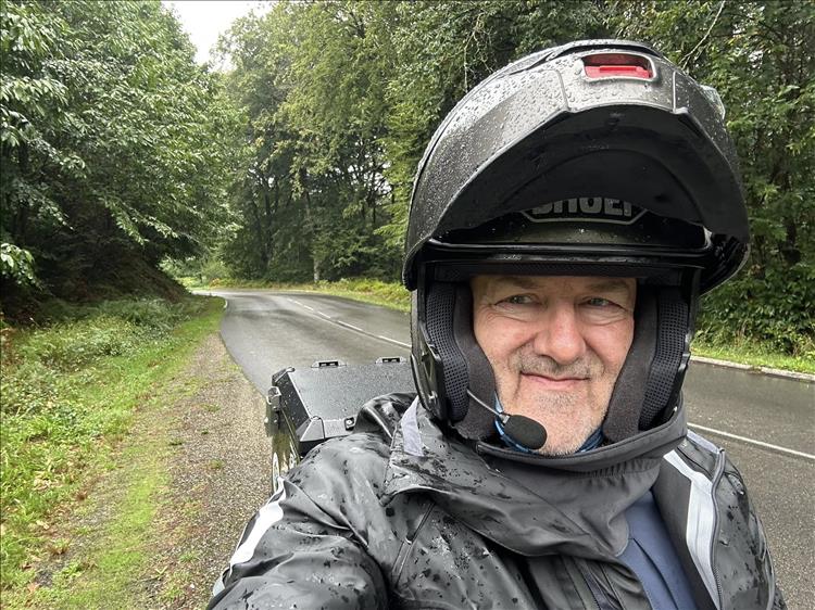 Selfie of Andy in his helmet in the rain in the trees but he's still smiling