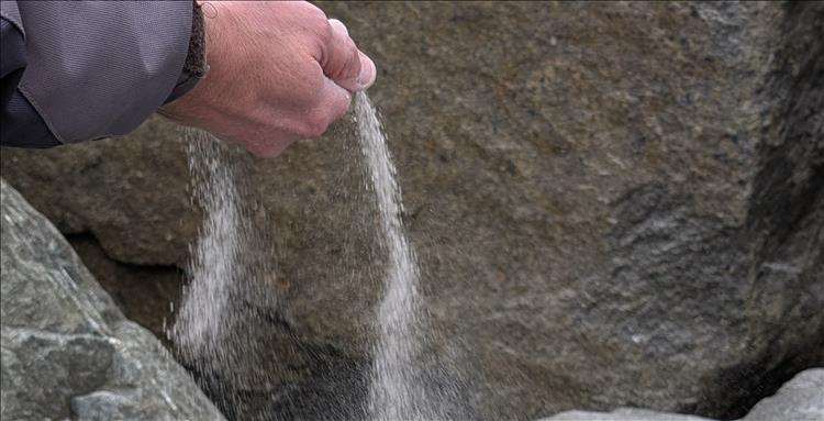 We see ashes pouring from a hand beside some rocks