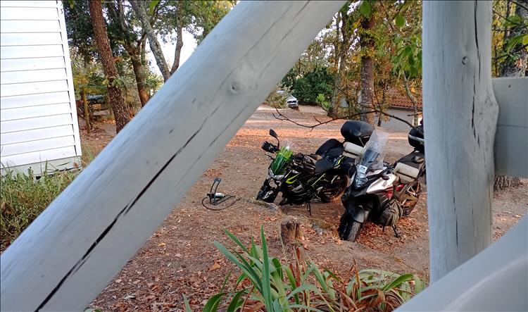 The 2 motorcycles framed by the woodwork of the shed. We can also see the footpump