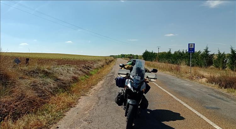 Ren's motorcycle with a long road, dry farmland and a few trees in Northern Spain