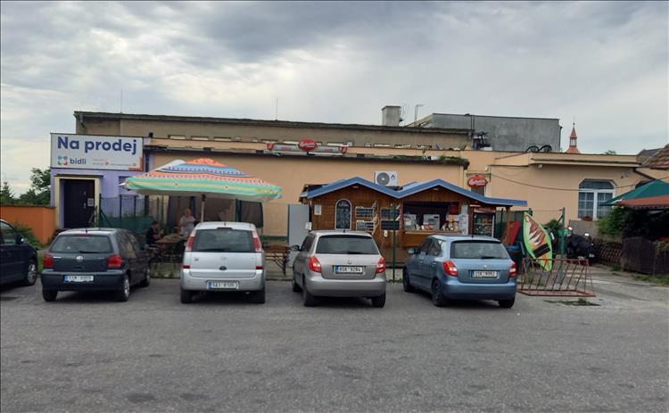A building with an outside hut serving as an outside counter, a few cars and a bench
