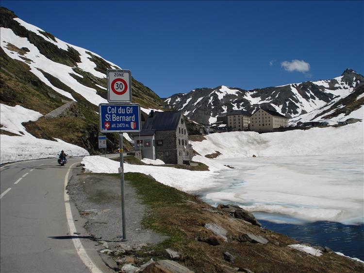 Snowy mountain top with a road and a motorcyclist passing along in an alpine scene