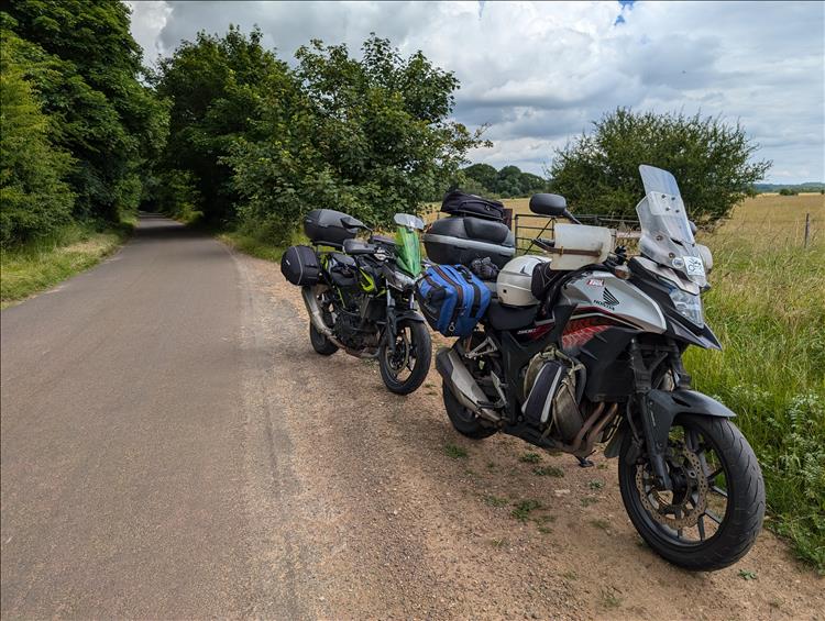 The bikes in among green trees, tan stalks of grass, hedgerows and fields