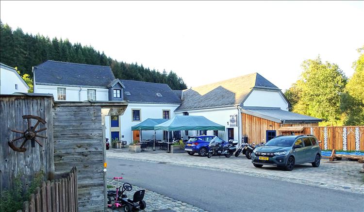 The courtyard of the hotel, white painted building, pine trees on the hill behind and the bike parked up