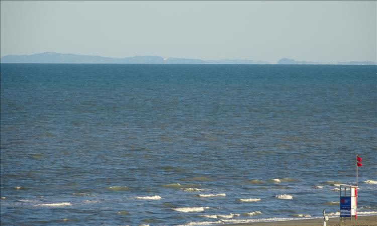 The edge of the beach, a stretch of calm ocean and more mountains in the hazy distance