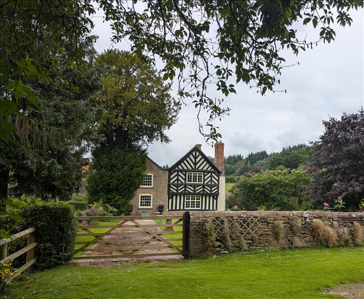 Between lush trees we see a timber framed tudor style house at Sollers Hope