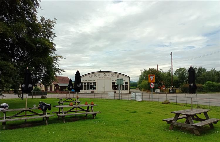 An old 40's style garage with Much Marcle Garage signage by a village green and trees