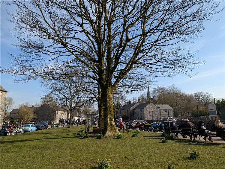 A large village green with motorcycles and their riders all around it.