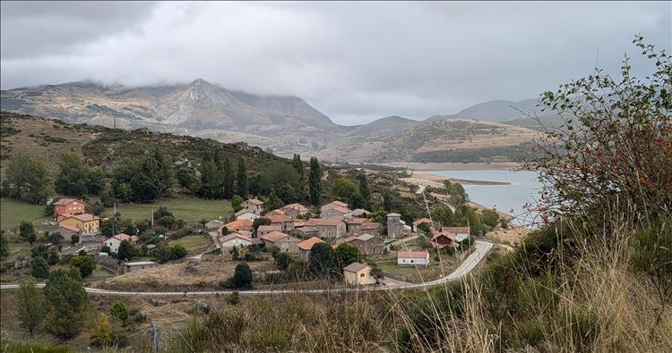 A small clump of maybe 20 or 30 houses by the side of a reservoir and mountains all around