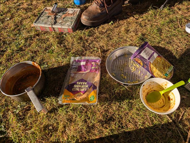 On the grass there's durty pans, bowls, empty packets and the remnants of the curry