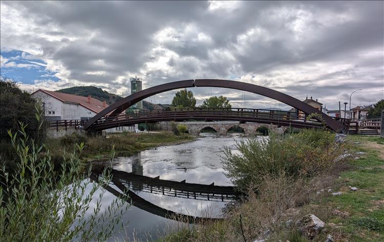 A steel stylish small footbridge and an old stone bridge cross the river next to the park