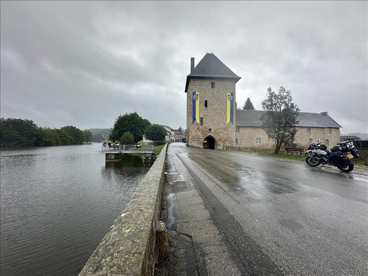 A river, a tall old stone building and a tarmac promonade under grey skies and rain