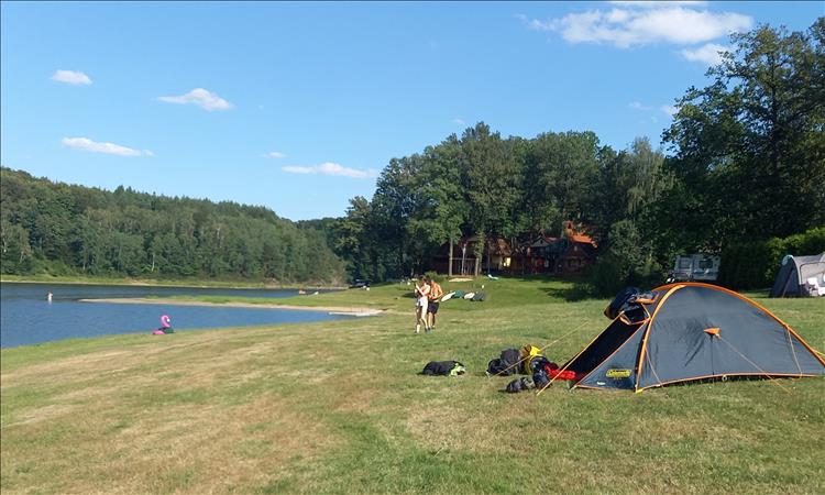 A grassy field, a few tent and the edge of a small lake at the campsite in Poland
