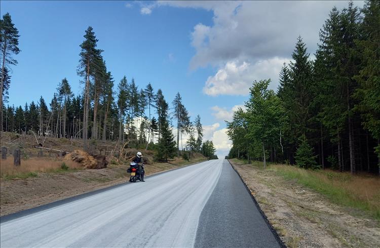 An empty road with freshly laid surface, a lone scooter and sunshine