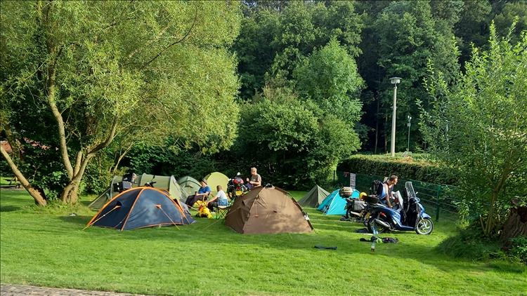 In the field there's several tents, small motorcycles, the campers enjoying their beer as the sun sets