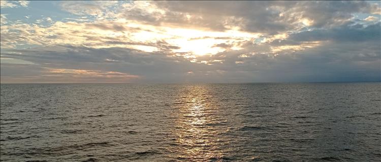 The sun is low in the sky and behind clouds over a calm sea off the coast of France