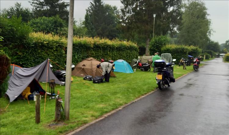 A line of tents and small motorcycles setting up camp in the rain