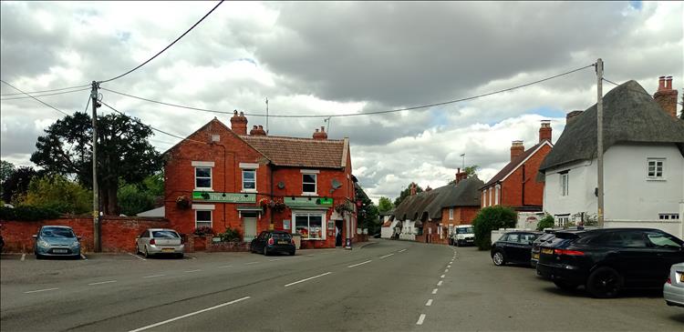 A brick built local shop next to some thatched cottages and a quiet road