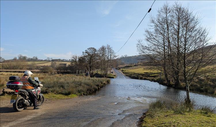 A small low river runs across the road, as Ren gets ready to turn his bike around