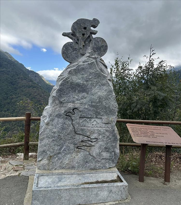 A stone obelisk with a cyclist carved into the top beside amazing mountain scenery