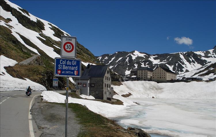 A winding road, alpine building and snowy mountain tops