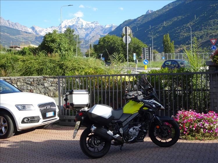 SV650 with luggage and an the jagged now capped mountains of The Alps