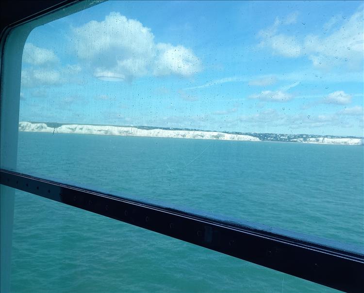 We see water and the white cliffs of Dover through a rather dirty ferry window